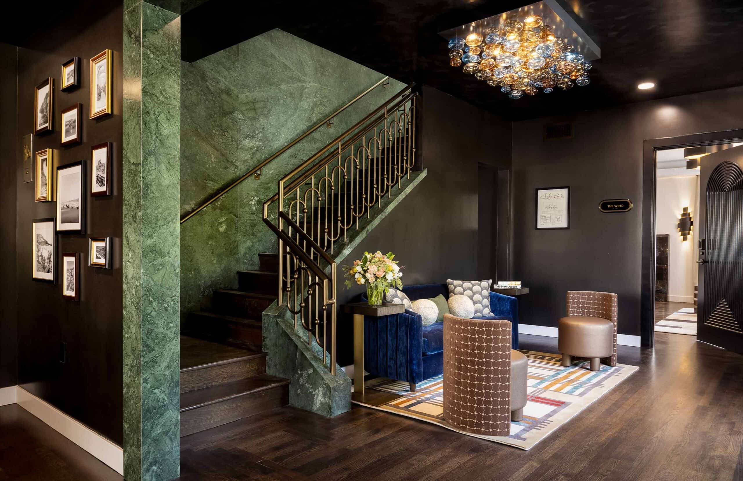 Elegant modern interior with a staircase, dark walls, contemporary seating area, and a crystal chandelier.