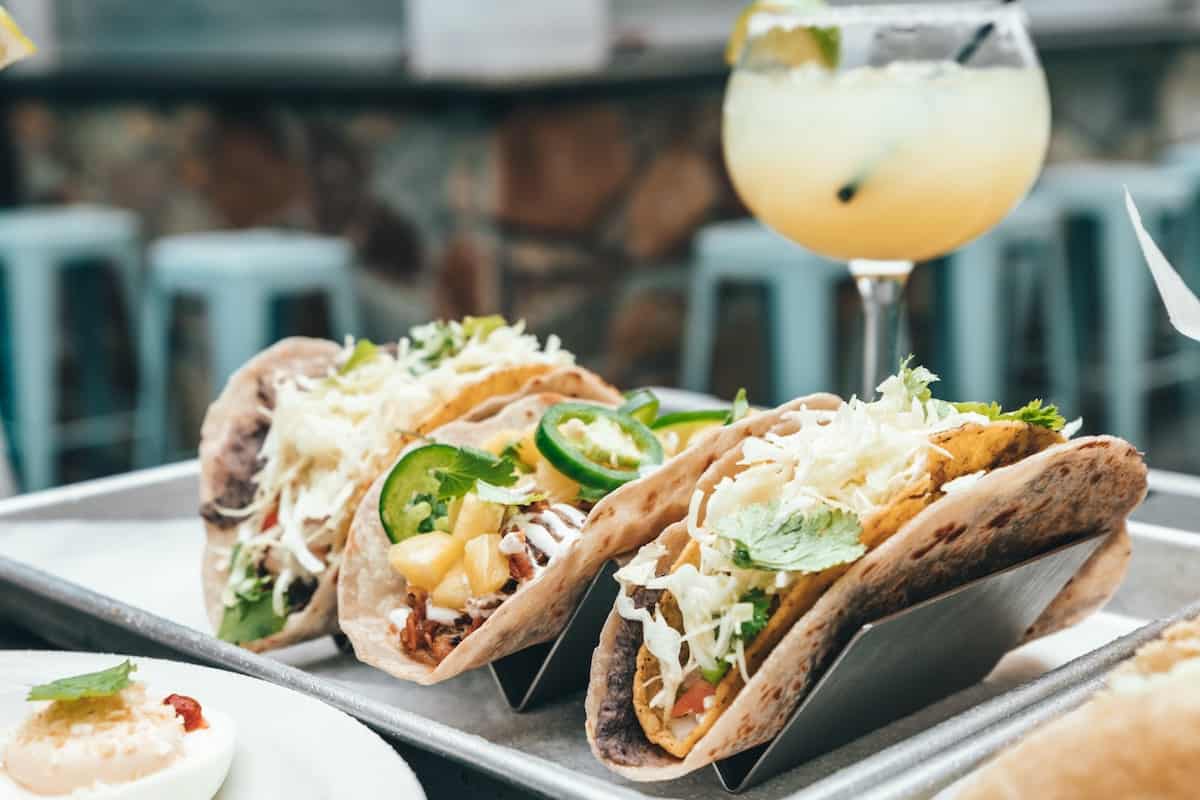 Plated fish tacos topped with cabbage slaw and sliced jalapeños, served with a refreshing citrus cocktail at a restaurant