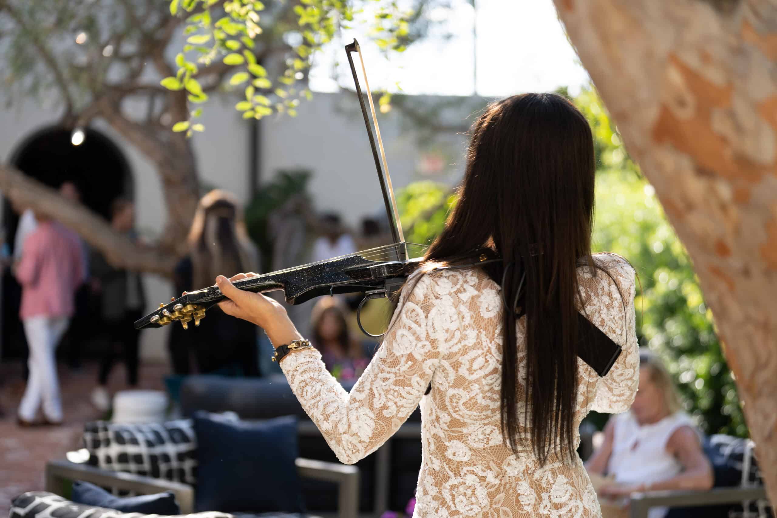 Woman playing the violin at an outdoor event, performing for guests in a sunlit garden setting.