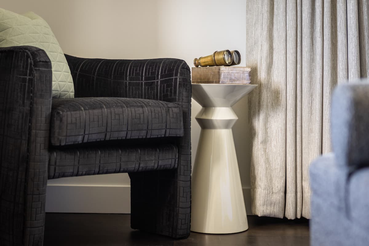 Modern accent side table with sculptural base beside a plush upholstered armchair in a refined living space