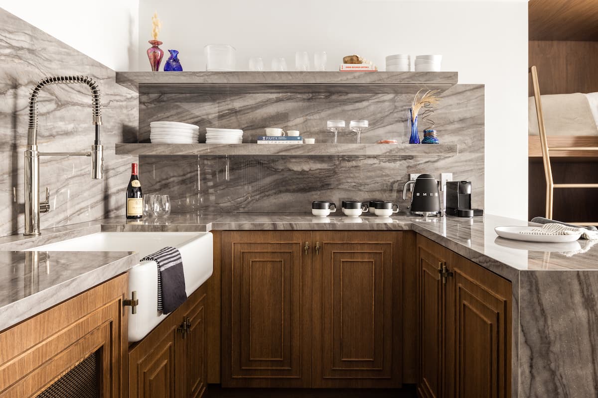 Modern kitchenette with marble countertops, wooden cabinetry, open shelving, and integrated sink in a luxury suite