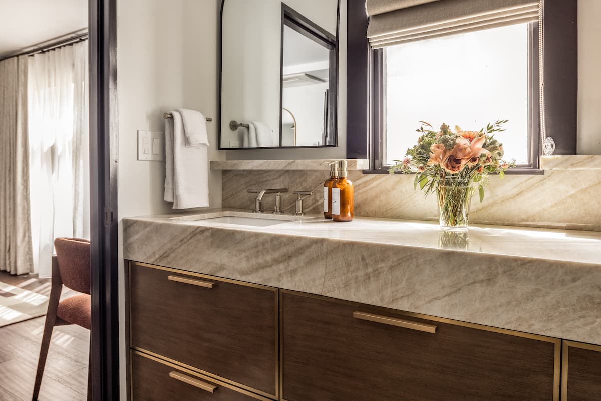 Luxury hotel bathroom vanity with marble countertop, modern fixtures, fresh flowers, and natural light from a window