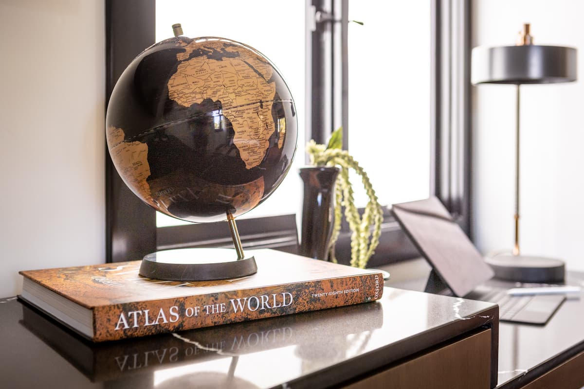 Decorative globe resting on a book titled “Atlas of the World” on a sleek desk near a window in a refined interior