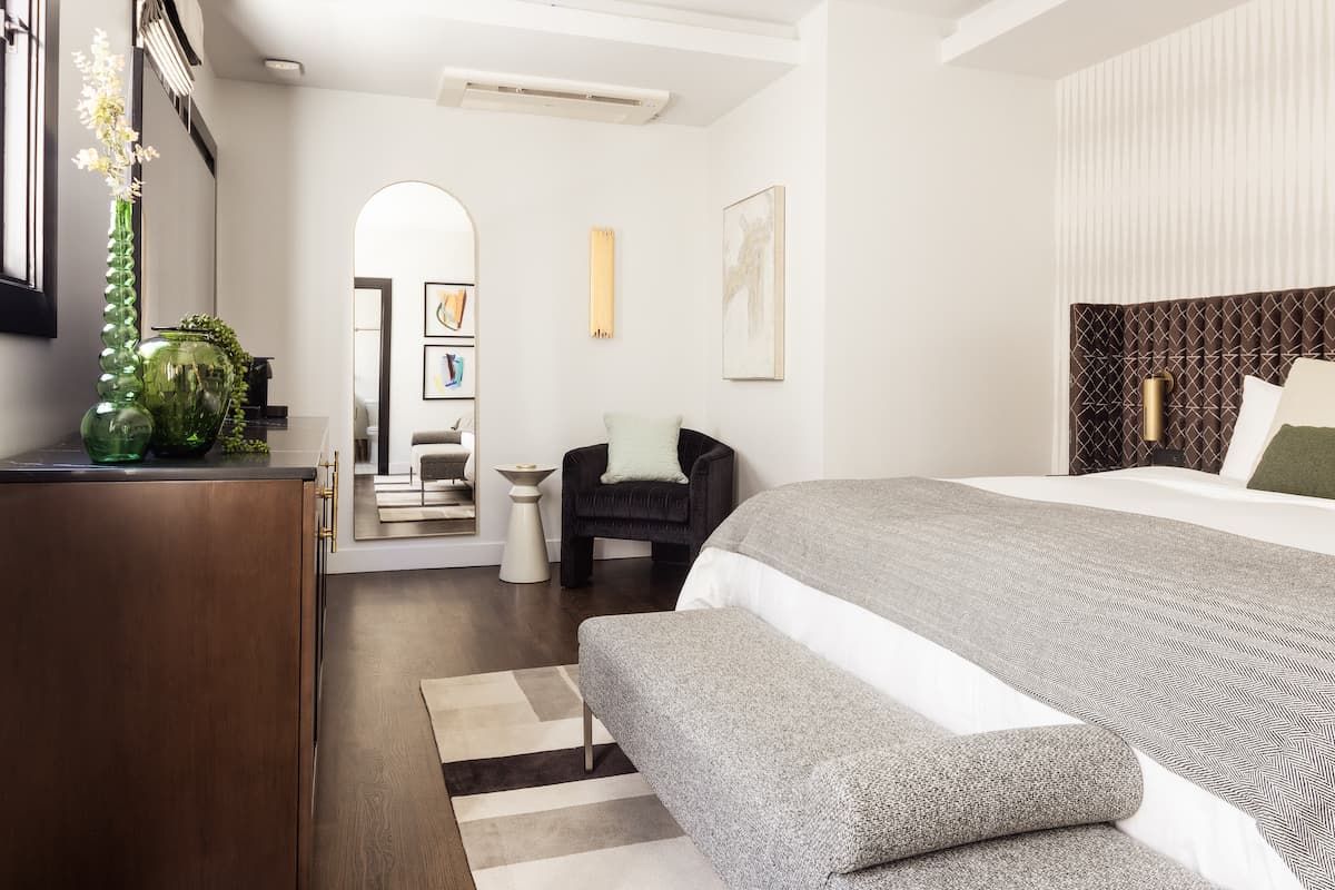 Bright luxury hotel bedroom with upholstered bed, sitting area, arched doorway, and minimalist modern décor