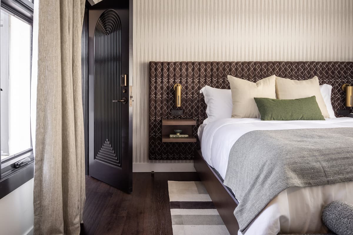 Luxury hotel bedroom with upholstered headboard, crisp white bedding, green accent pillows, and modern bedside lighting