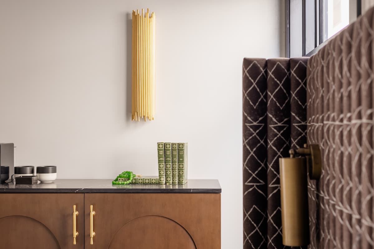 Modern hotel room detail with wood cabinetry, brass hardware, textured wall paneling, and minimalist decorative accents