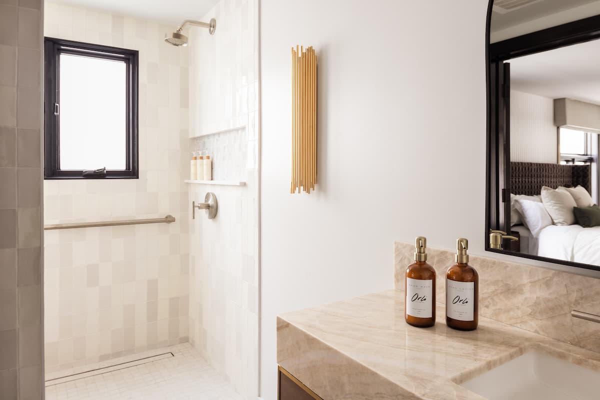 Bright hotel bathroom with walk-in shower, marble vanity, arched mirror, and minimalist luxury toiletries