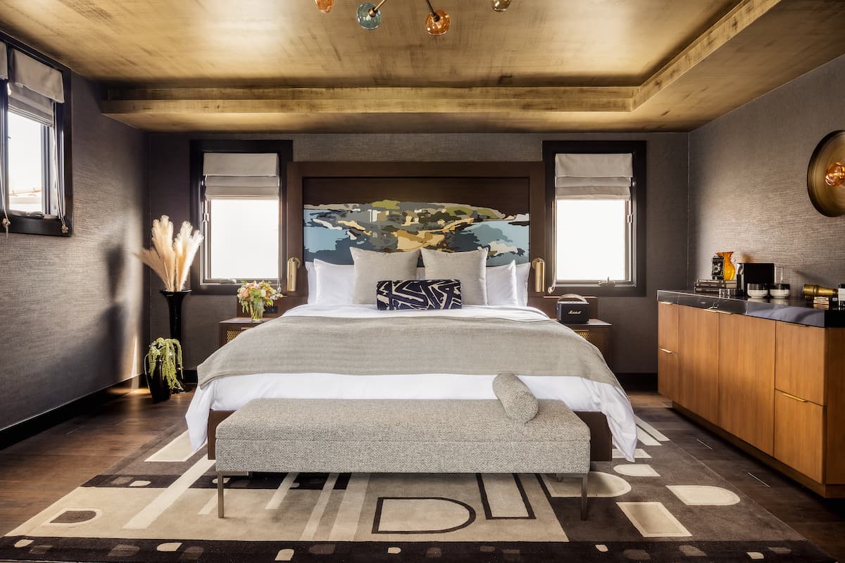 Luxury hotel bedroom with king-size bed, artistic headboard, warm wood furnishings, and sophisticated ambient lighting