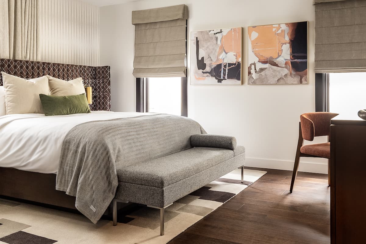 Luxury hotel bedroom with king-size bed, upholstered bench, abstract wall art, and warm modern furnishings