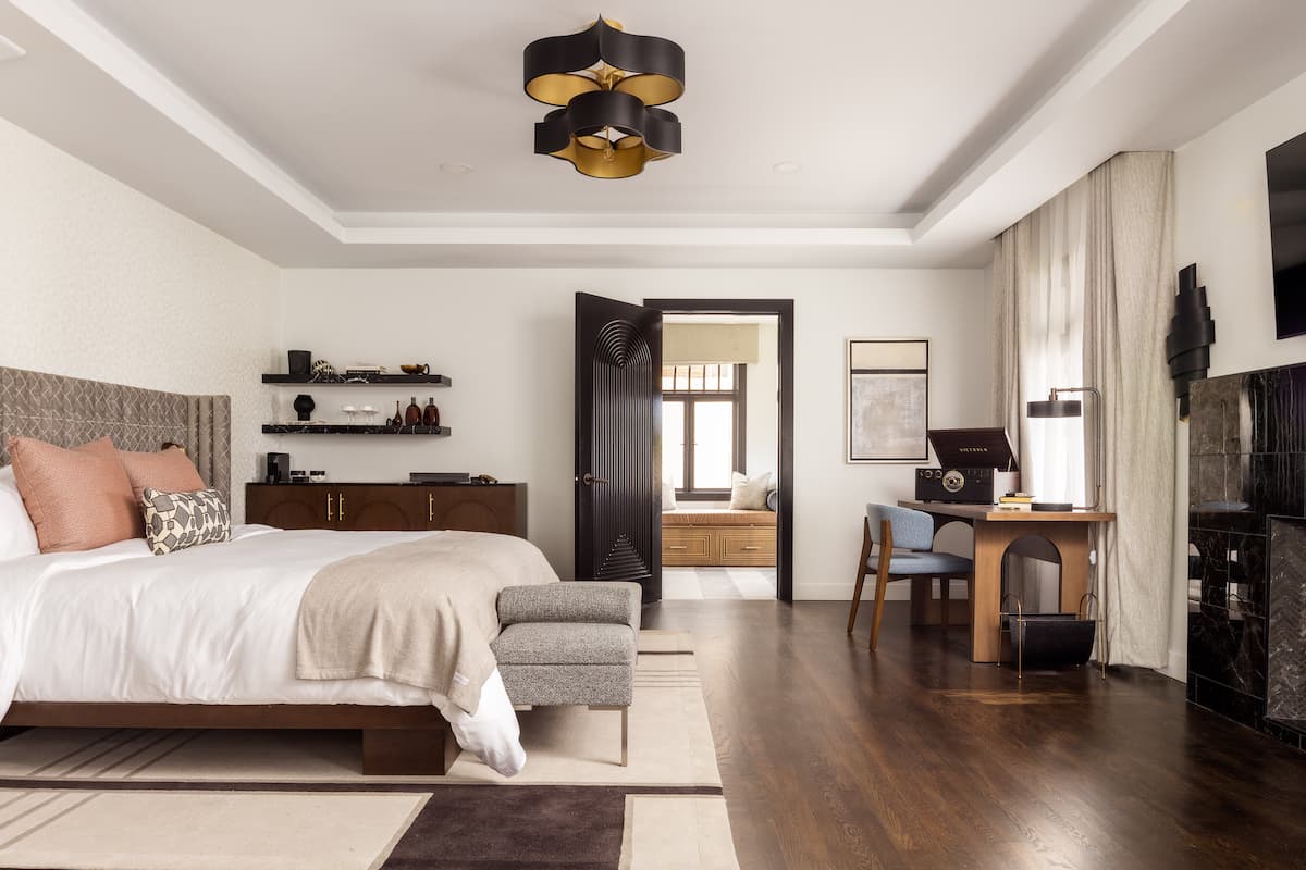 Spacious luxury hotel suite featuring a king-size bed, sitting area, writing desk, and elegant modern décor with warm natural light