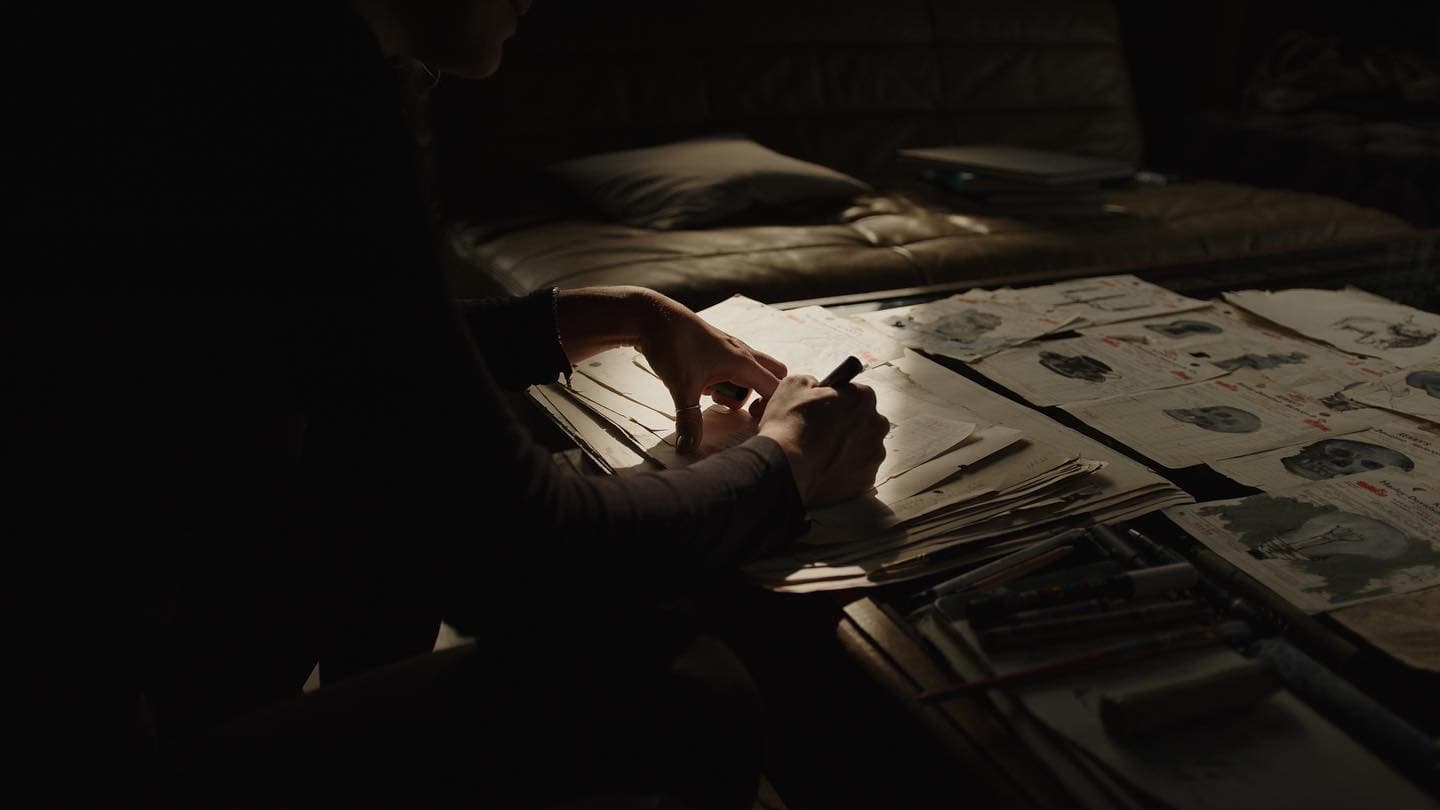 Artist working late at a desk, surrounded by illustrated pages and design sketches.