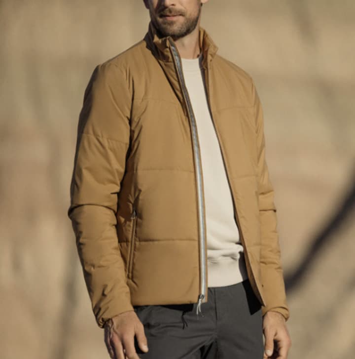 Man wearing a tan quilted jacket layered over a white shirt, styled for a modern casual outdoor look