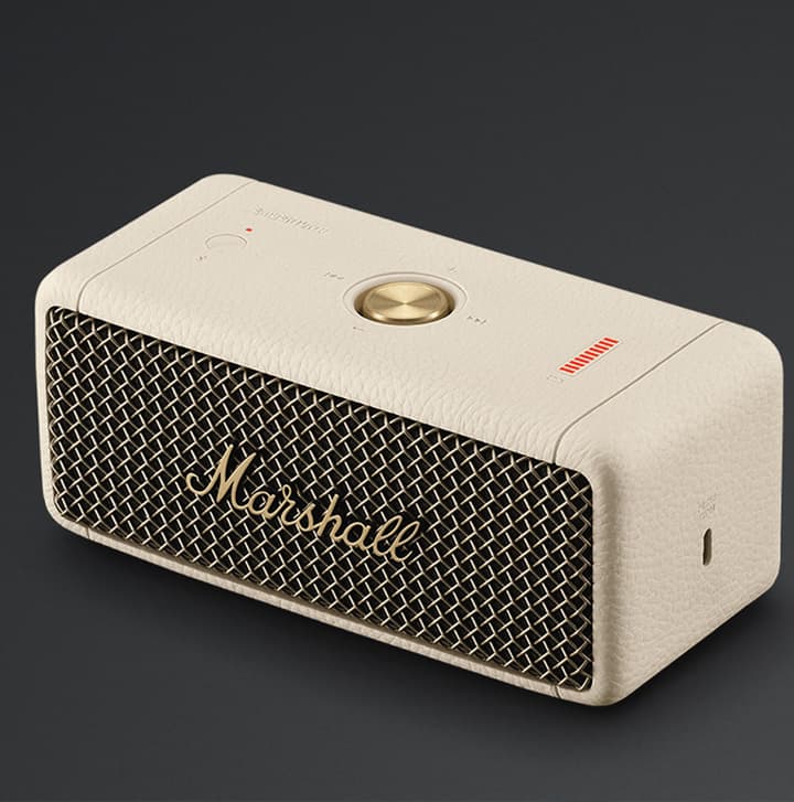 Cream-colored Marshall portable Bluetooth speaker with gold accents displayed on a dark background
