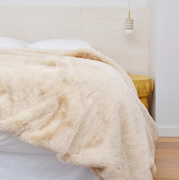 Soft beige faux fur throw draped over a neatly made bed in a calm, modern bedroom interior