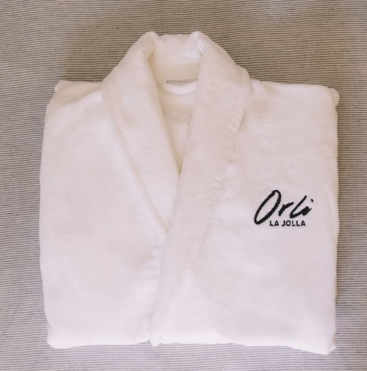 Plush white bathrobe embroidered with the Orli La Jolla logo, neatly folded on a soft neutral surface
