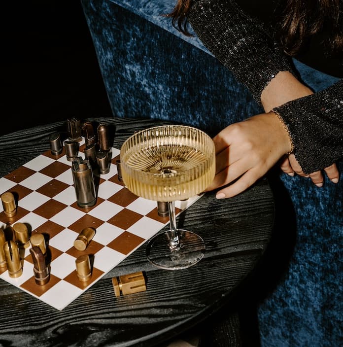 A person playing chess and having a drink from a coupe cocktail glass