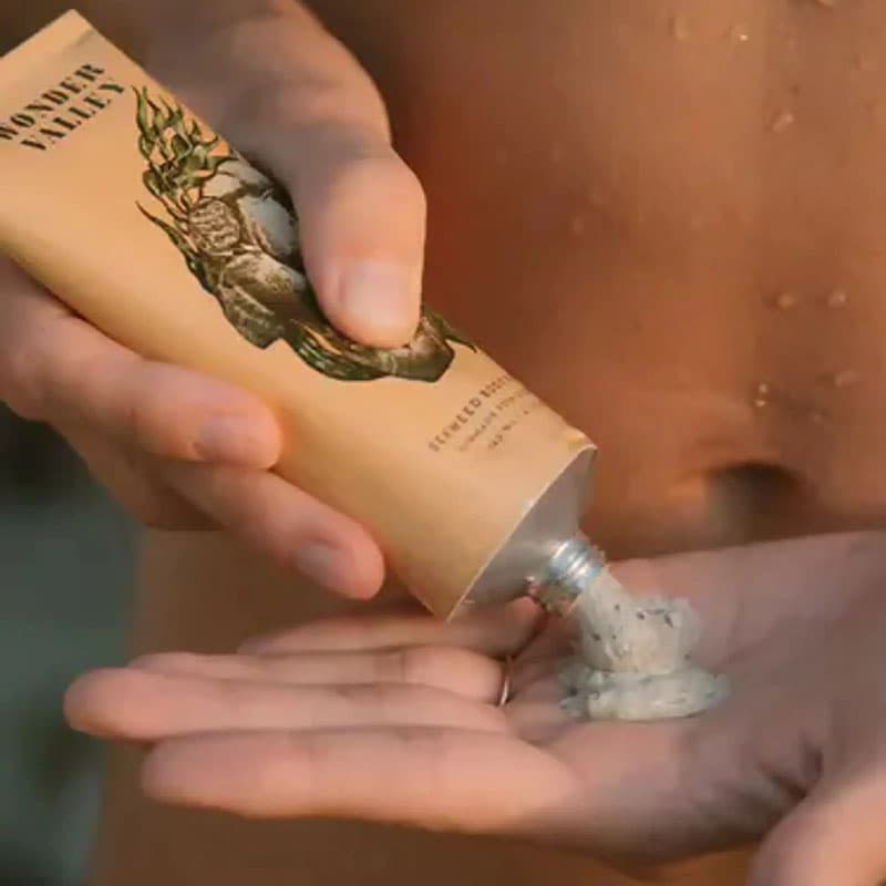 Person dispensing natural exfoliating body scrub from eco-friendly tube into their hand, highlighting clean skincare and self-care routine.