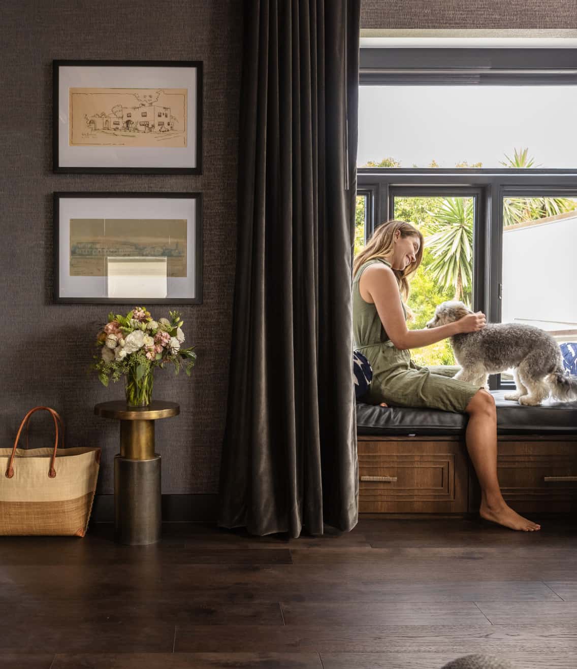 Woman sitting by a window seat petting a dog in a serene, well-appointed home or hotel interior with natural light
