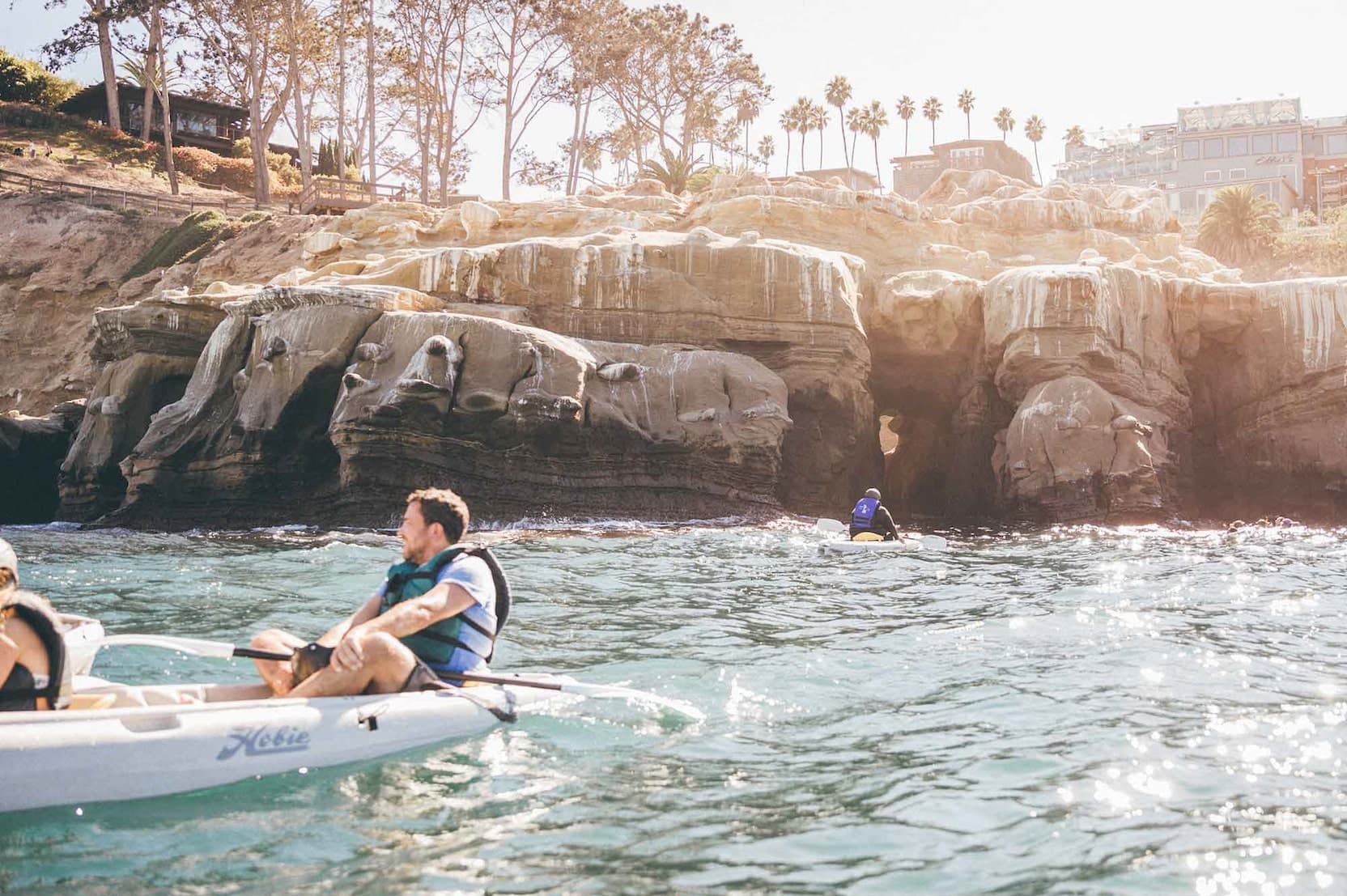 Guest kayaking along a scenic rocky coastline, enjoying an active ocean experience in clear blue water