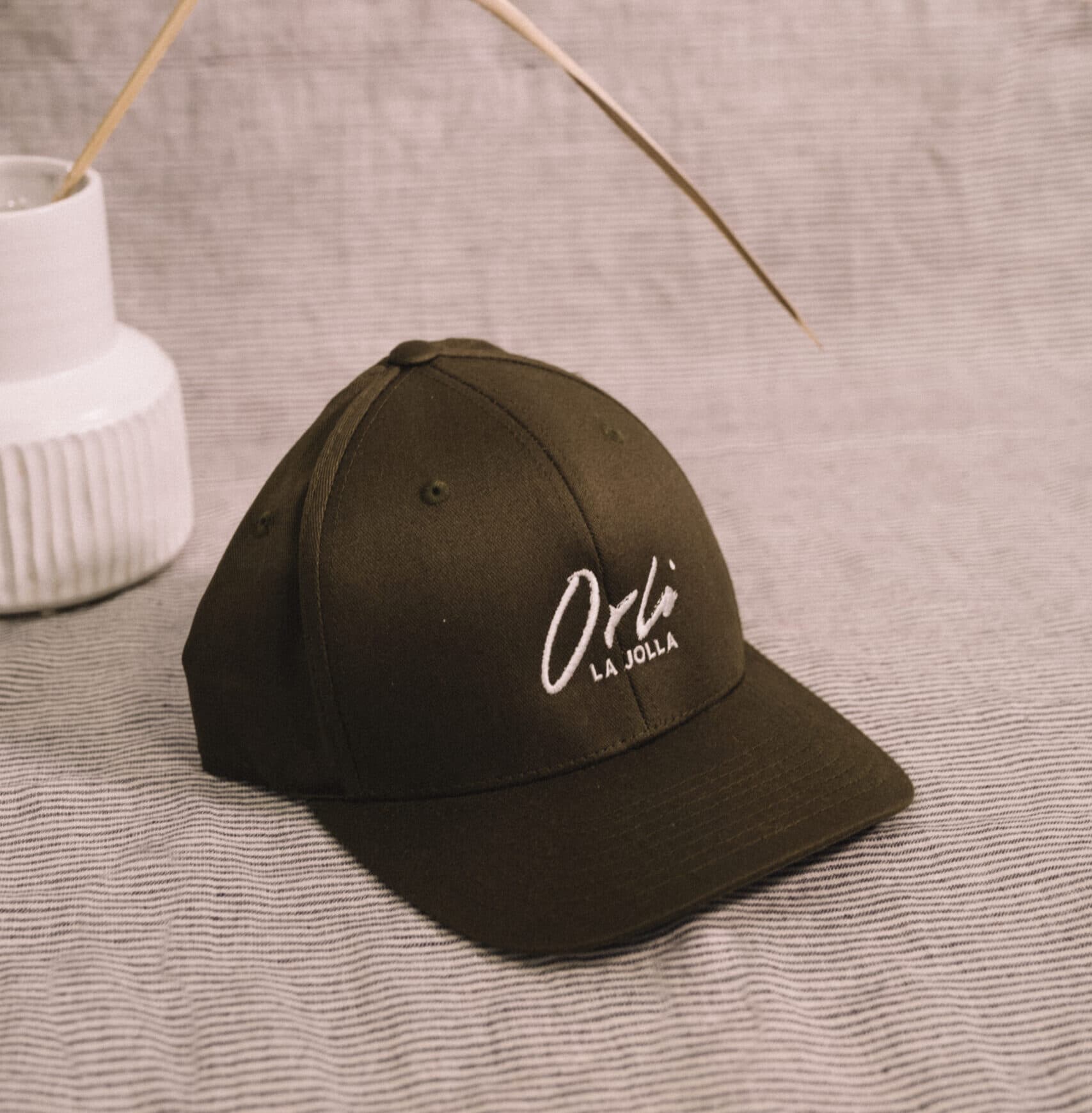 Olive green Orli La Jolla baseball cap with embroidered white logo, styled on a neutral textured surface