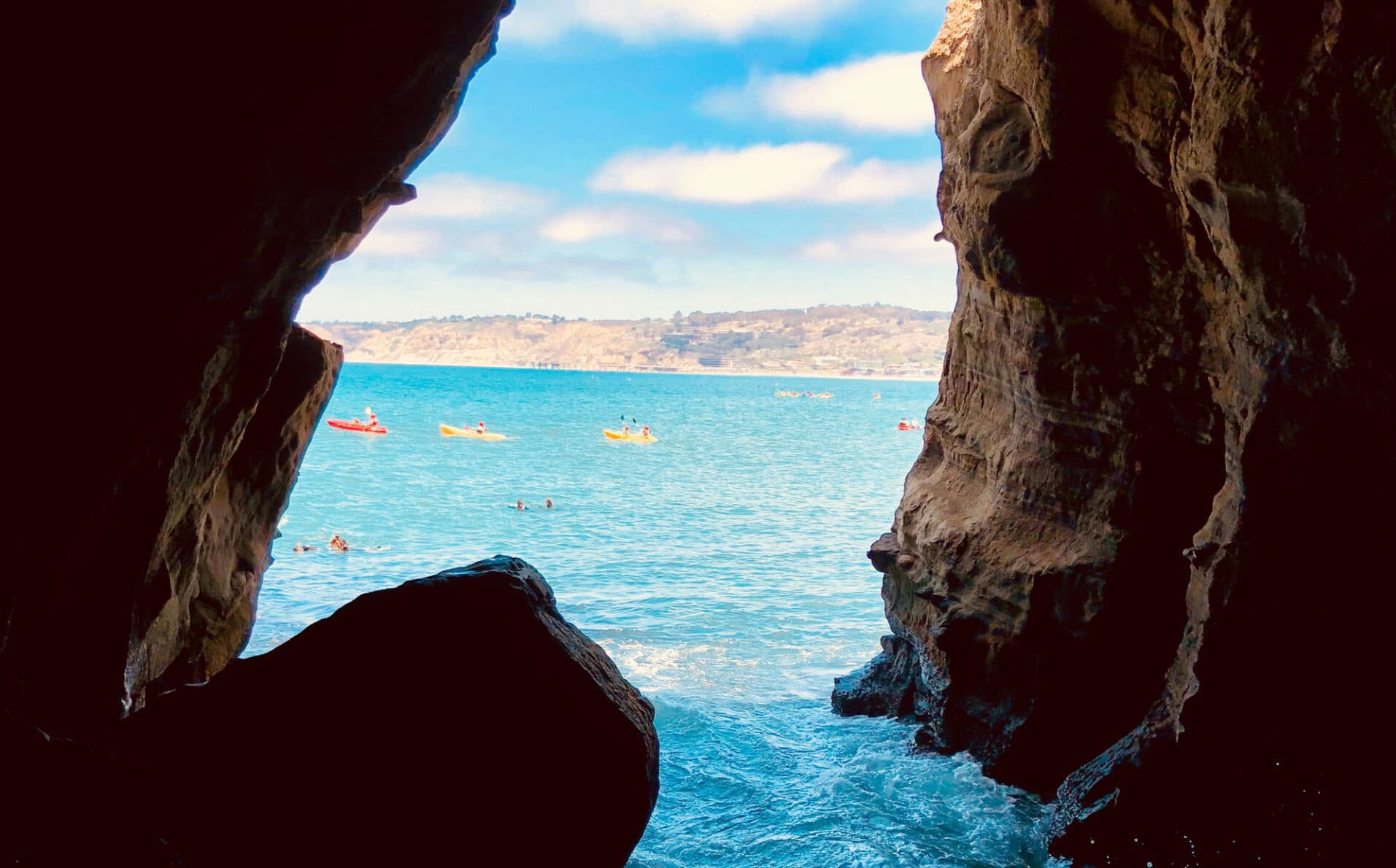 View of turquoise ocean and kayakers seen through a rocky coastal cave opening on a sunny day