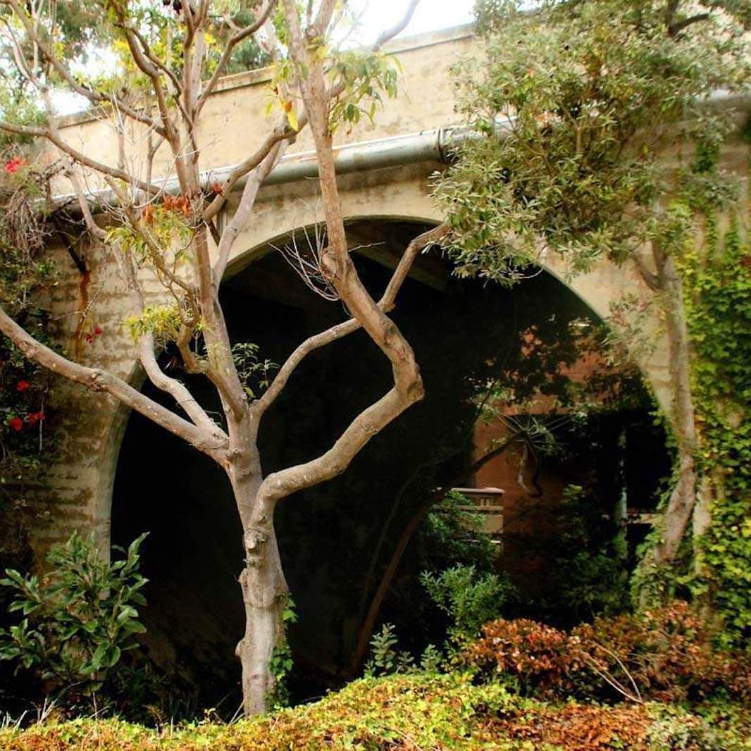 Stone archway surrounded by mature trees and lush garden landscaping in a serene outdoor courtyard