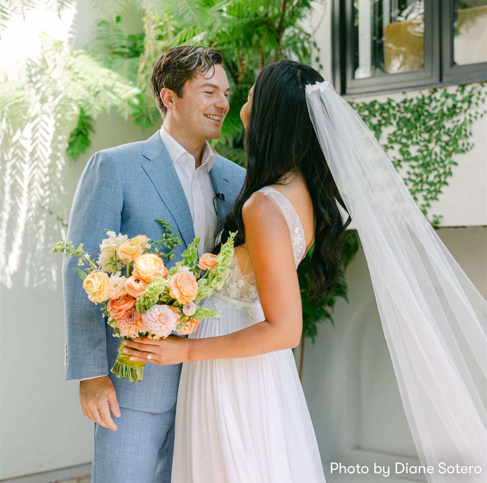 Bride and groom smiling at each other outdoors as the bride holds a bouquet of flowers