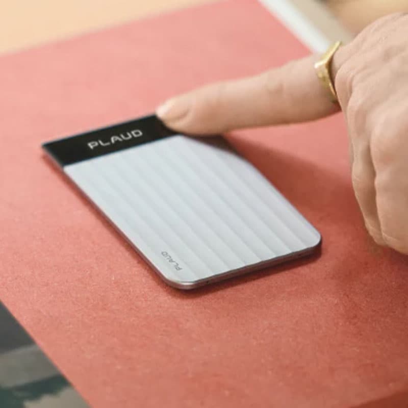 Close-up of a person using a compact Plaud smart note-taking device on a desk, showcasing a minimalist digital recorder designed for productivity, meetings, and voice notes.