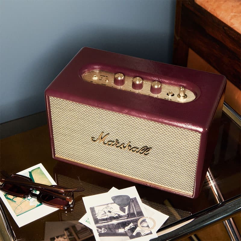 Vintage Marshall speaker with burgundy casing and gold control panel displayed on a side table, styled with classic photographs and personal accessories for a retro interior aesthetic.